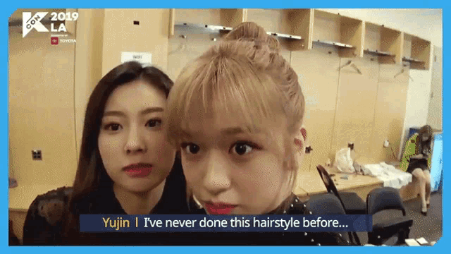 two women are standing next to each other in a locker room and one of them is talking about her hairstyle .