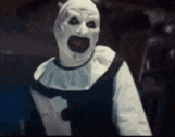 a scary clown is wearing a white mask and a black and white outfit .