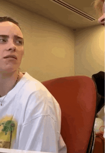 a woman in a white shirt is sitting in a red chair and making a face .