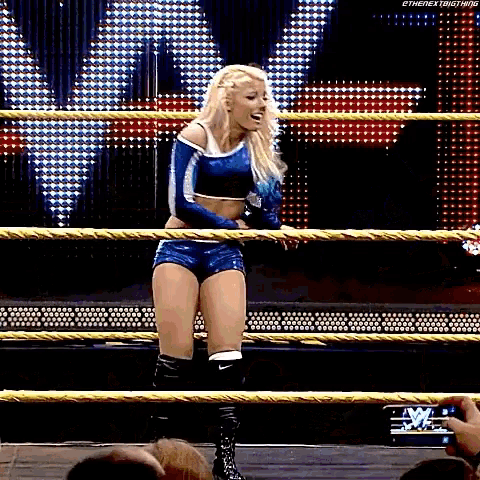 a female wrestler is standing in a roped in wrestling ring .