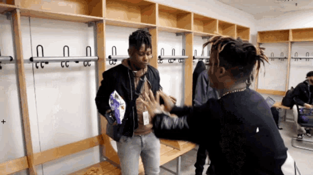 a man holding a bag of chips talks to another man in a changing room