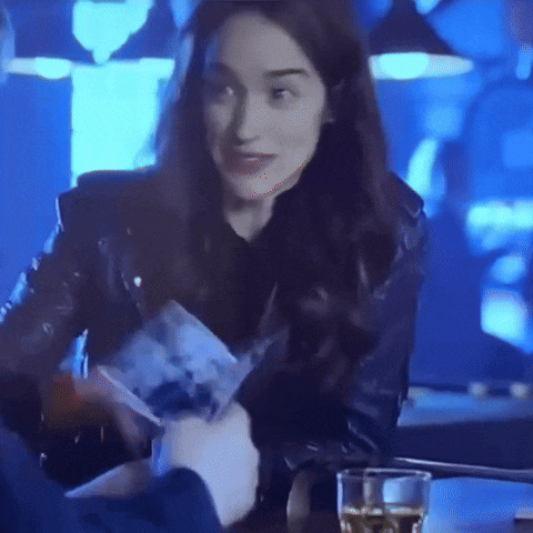 a woman in a black leather jacket is sitting at a table with a glass of whiskey .