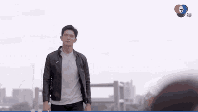 a man in a black jacket is walking in front of a tv screen that says 7