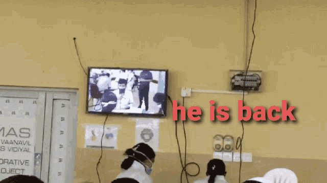 a group of people are sitting in front of a television that says he is back