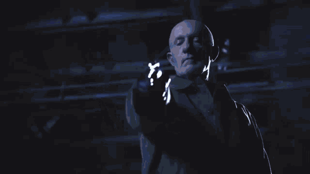 a bald man in a suit is holding a blue light in his hand .