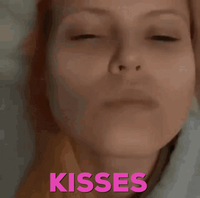 a woman with red hair is laying in a bed with the word kisses above her head