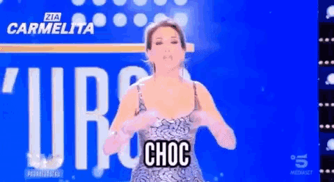 a woman in a silver dress is standing in front of a blue screen that says zia carmelita
