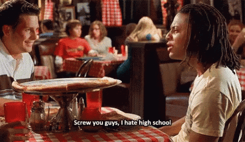 a man is sitting at a table with a pizza and says screw you guys i hate high school