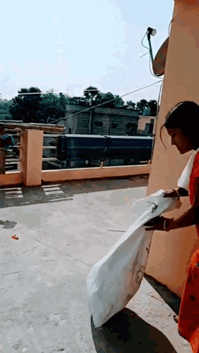 a woman in a red sari is standing on a rooftop holding a white bag .