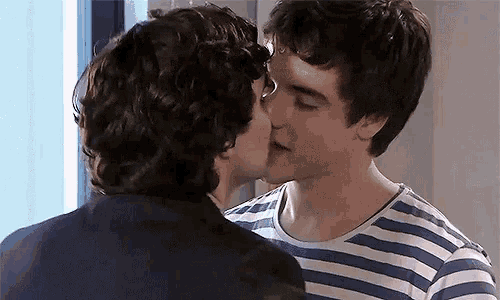 two young men are kissing in front of a window