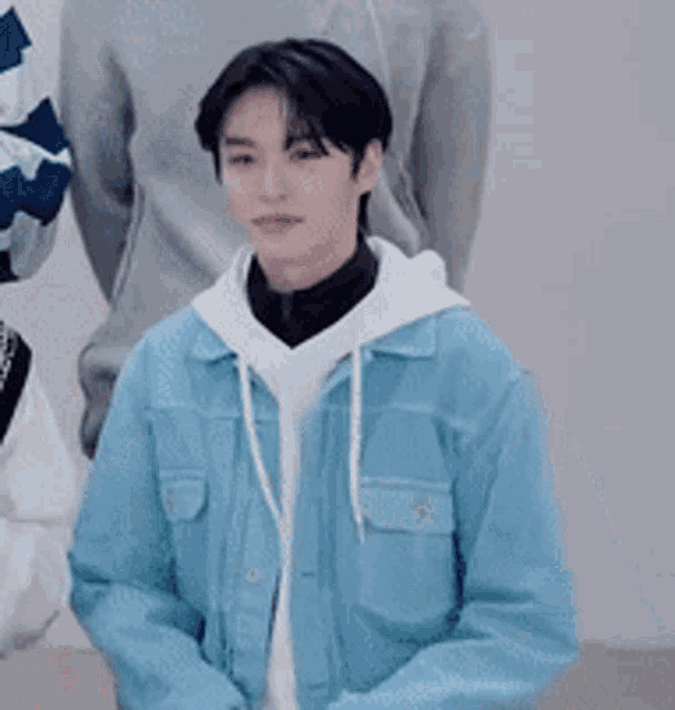 a young man wearing a blue jacket and a white hoodie is sitting with his arms crossed .