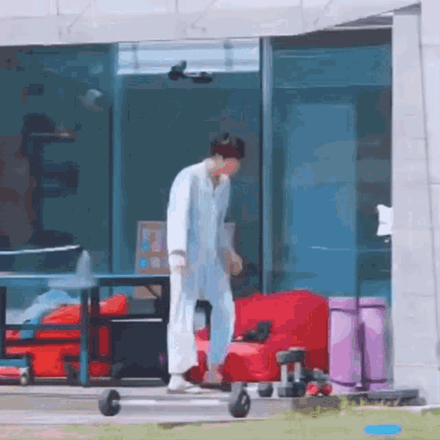 a man in a white robe is walking in front of a building with a red chair and a purple suitcase .