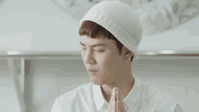 a young man wearing a white beanie and a white shirt is praying