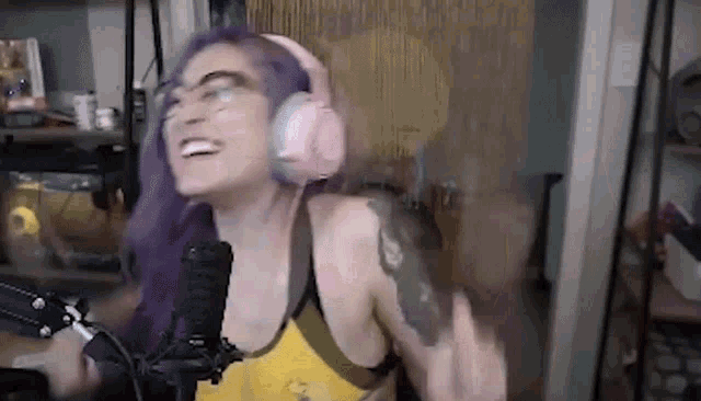 a woman with purple hair is wearing pink headphones and a yellow tank top .