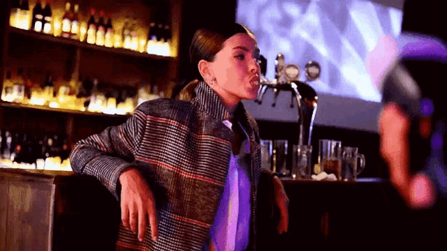 a woman wearing a plaid jacket is standing in front of a bar