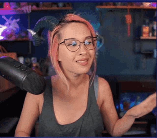 a woman wearing glasses and a horned headband stands in front of a microphone