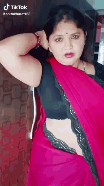 a woman in a red saree is standing in front of a wall .