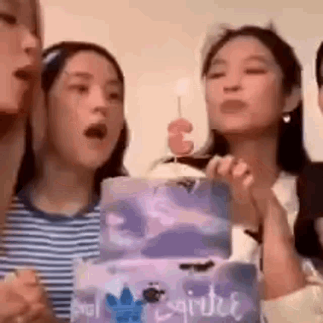 a group of women are standing around a birthday cake with a candle .