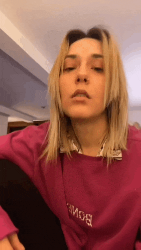 a woman with blonde hair is wearing a pink sweater and a nose ring .