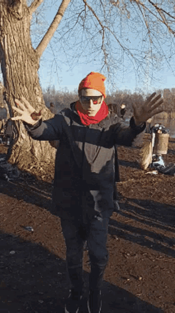 a man wearing an orange hat and scarf is standing in front of a tree