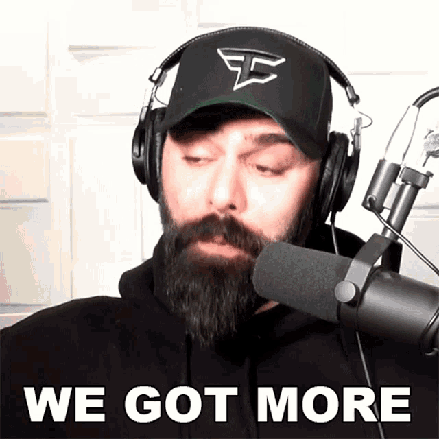 a man with a beard wearing headphones stands in front of a microphone and says we got more