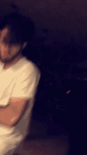 a blurry picture of a man in a white shirt standing in a dark room .