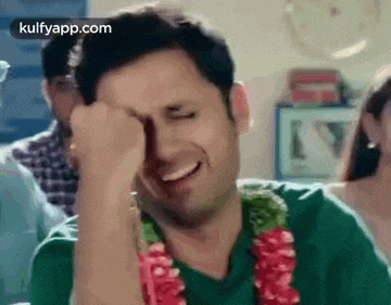 a man is laughing and covering his face with his fist while wearing a garland around his neck .