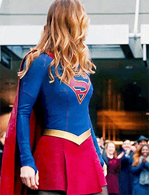 a woman in a blue and red superman costume is standing in front of a crowd .