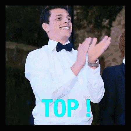 a man in a tuxedo is clapping his hands in front of a sign that says " top "