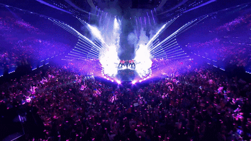 a group of people are dancing on a stage with purple lights