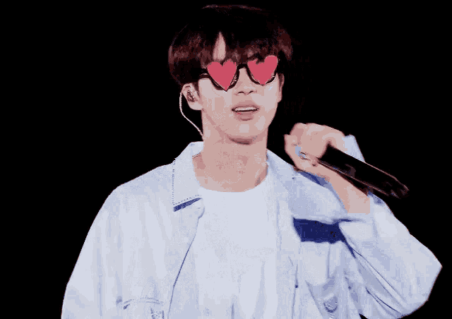a young man wearing heart shaped sunglasses holds a microphone
