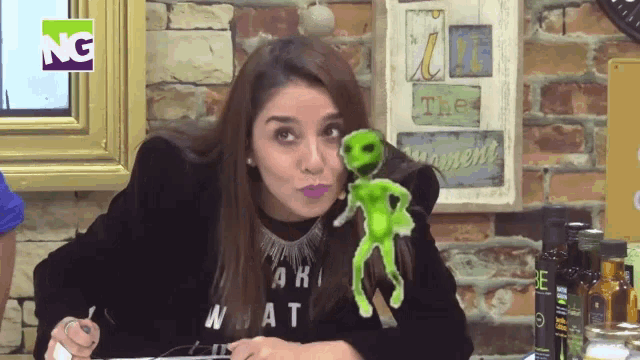 a woman holding a stuffed green alien in front of a sign that says ng on it