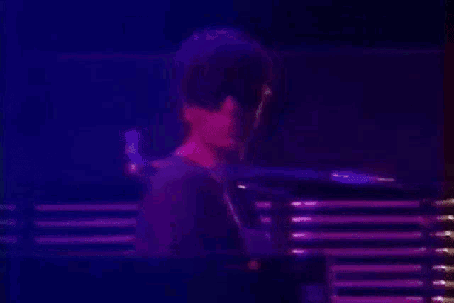 a man is playing a keyboard in a dark room with a blue light behind him
