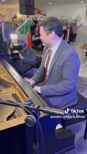 a man in a suit and tie is playing a piano in front of a crowd