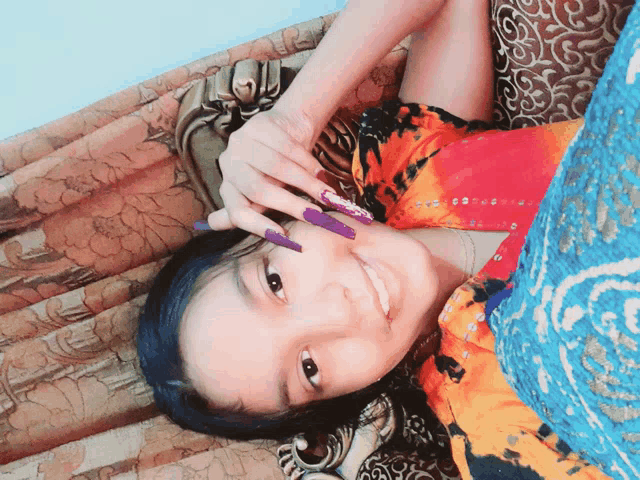 a girl with long purple nails is laying on a couch and smiling
