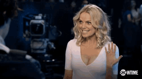 a woman in a white shirt is smiling and waving in front of a showtime camera .