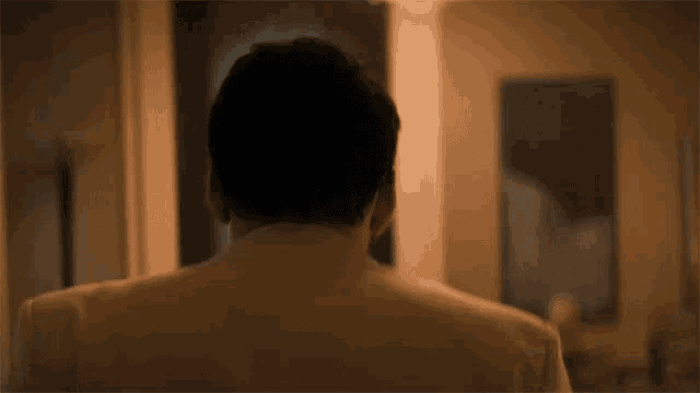 the back of a man 's head is shown in a room with a painting in the background .