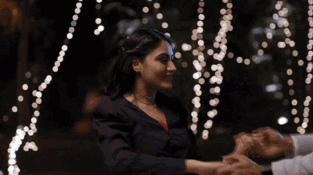 a man and a woman are holding hands in front of string lights