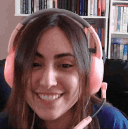a woman wearing pink headphones and a microphone smiles for the camera