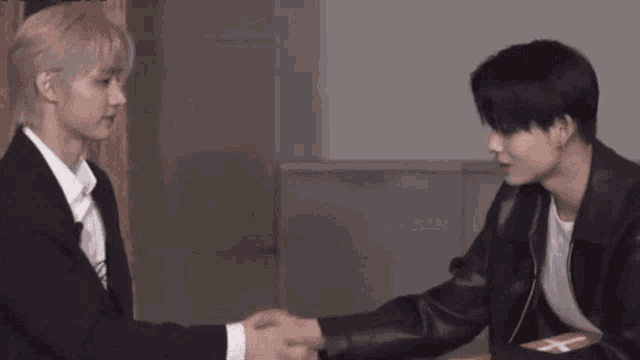 two men are shaking hands while sitting next to each other in a room .