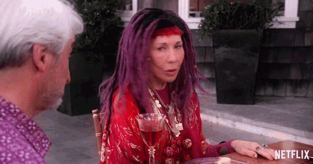 a woman with purple hair is sitting at a table with a netflix logo