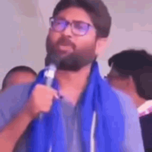 a man with a beard and glasses is holding a microphone and speaking into it .