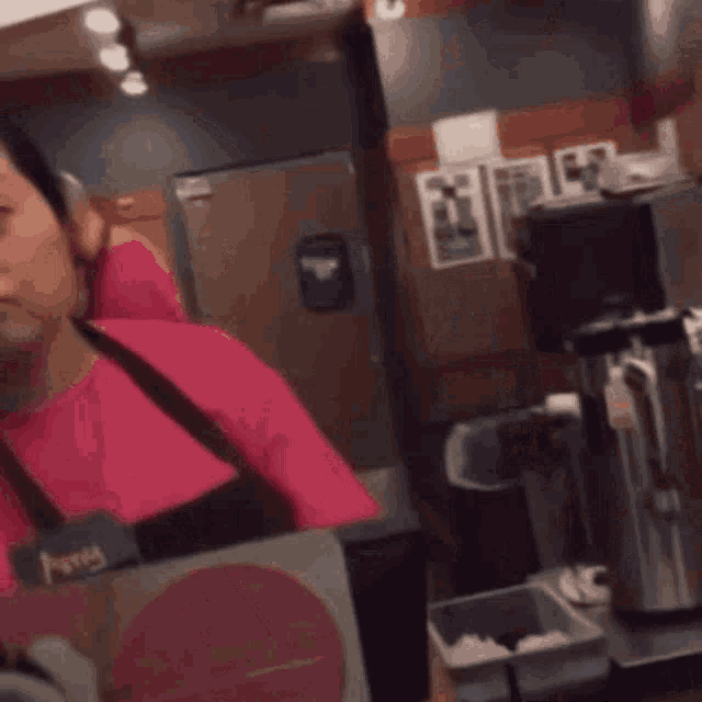 a woman in a pink shirt and apron is making a funny face in a kitchen .