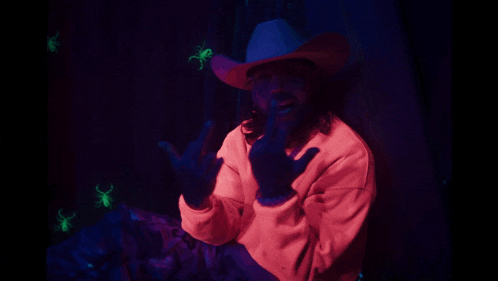 a man in a cowboy hat is giving the middle finger in front of glowing insects
