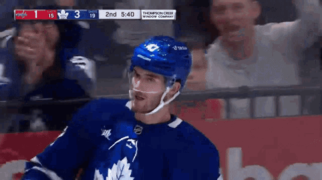 a hockey player wearing a maple leafs jersey stands in front of a scoreboard