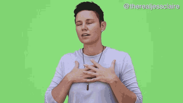 a woman is holding her hands on her chest in front of a green screen .