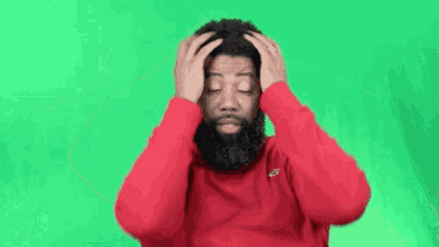a man with a beard wearing a red sweater is holding his head .