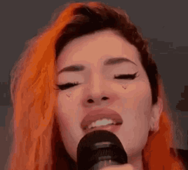a close up of a woman singing into a microphone with her eyes closed .