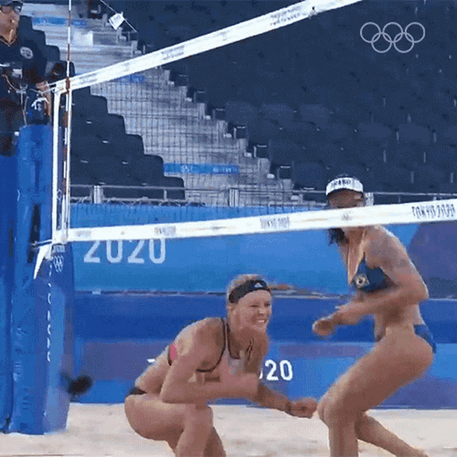 two women playing volleyball in front of a net that says tokyo 2020
