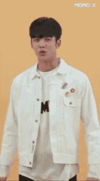 a young man wearing a white jacket and a white shirt is standing in front of a yellow background .